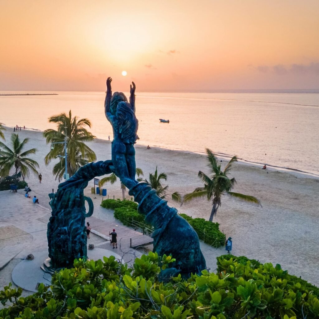Stunning sunset view at Portal Maya sculpture, Playa del Carmen beachside with palm trees and serene sea.